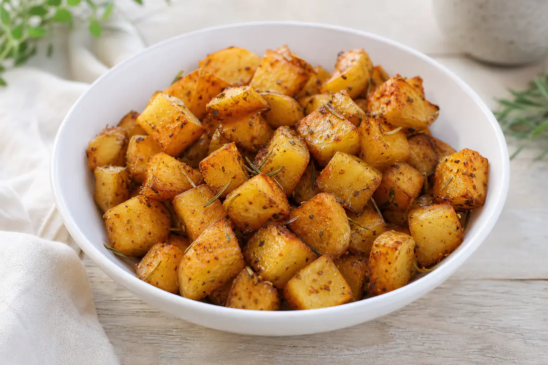 Goudbruine aardappelblokjes met rozemarijn en grof zout in een witte schaal