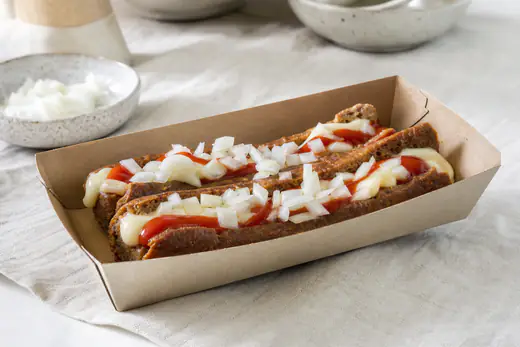 Twee bruingebakken frikandellen speciaal met curry, frietsaus en gesnipperde ui in een kartonnen bakje