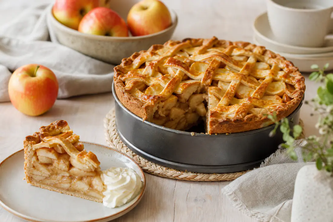 Hollandse appeltaart met deegrooster en een aangesneden punt op een bordje met slagroom