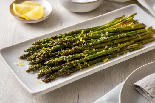 Geroosterde groene asperges met citroenrasp en grof zout op een langwerpige witte schaal