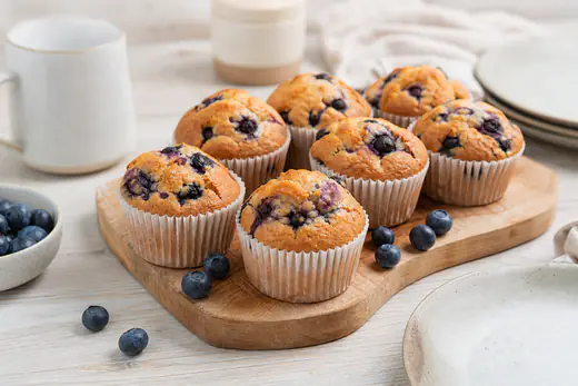 Goudbruine blauwe bessen muffins in papieren vormpjes op een houten plank met losse bessen