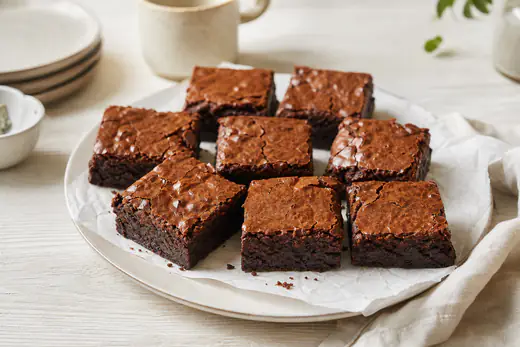 Vierkante chocoladebrownies met een glanzend korstje en een smeuïge kern op bakpapier