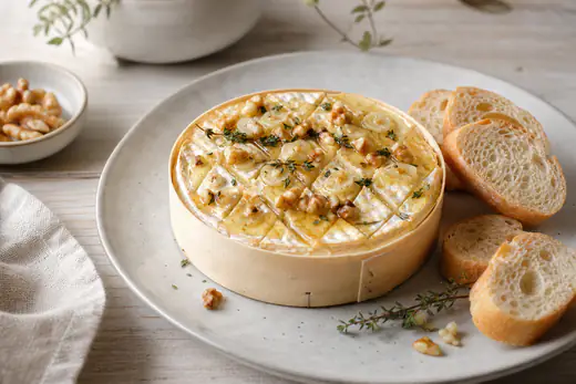 Hele gebakken camembert in een houten doosje met honing, tijm en walnoten, omringd door stukjes stokbrood om te dippen
