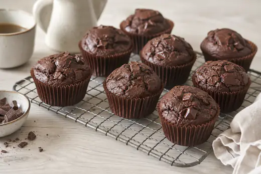 Chocolademuffins met bolle bovenkant en gesmolten chocoladestukjes in papieren vormpjes op een rooster