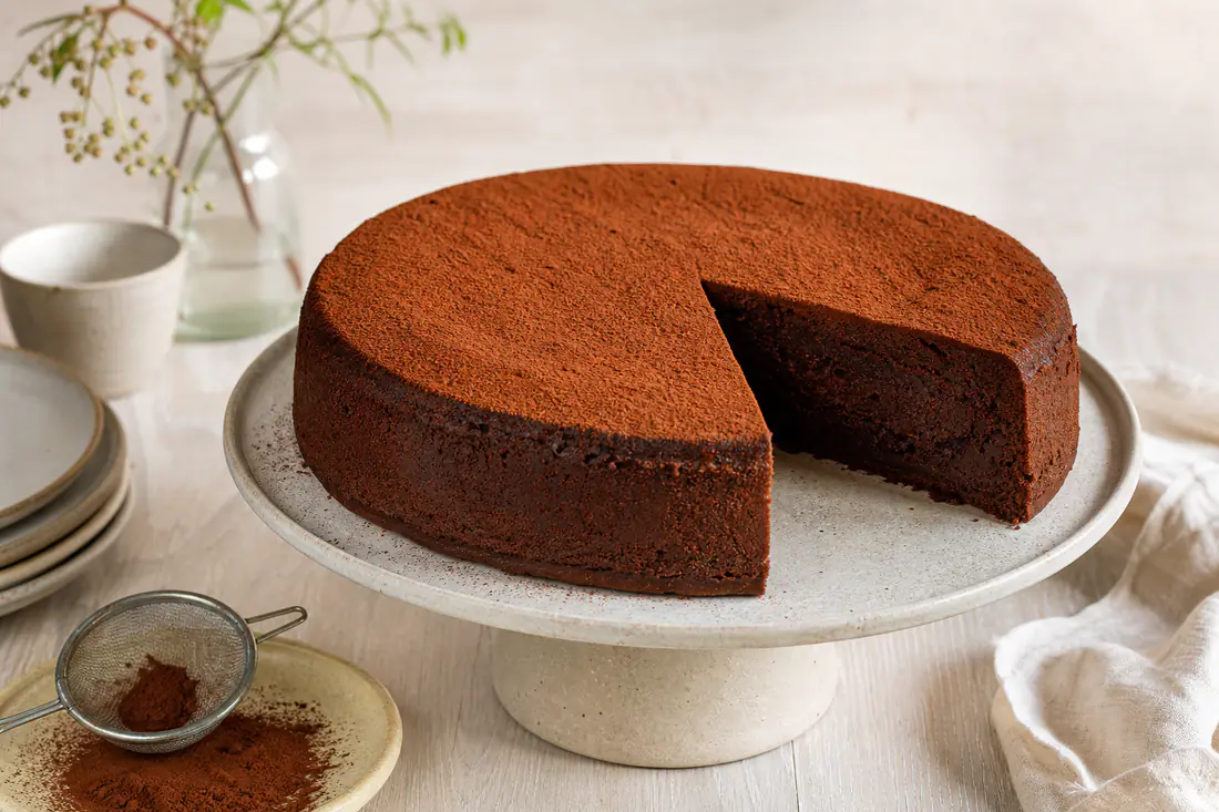 Ronde chocoladetaart met een punt eruit gesneden en cacaopoeder erover op een taartplateau