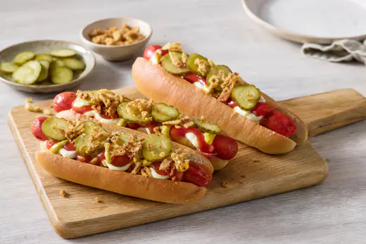 Rode Deense worstjes in hotdogbroodjes met remoulade, gebakken uitjes en plakjes augurk op een houten plank