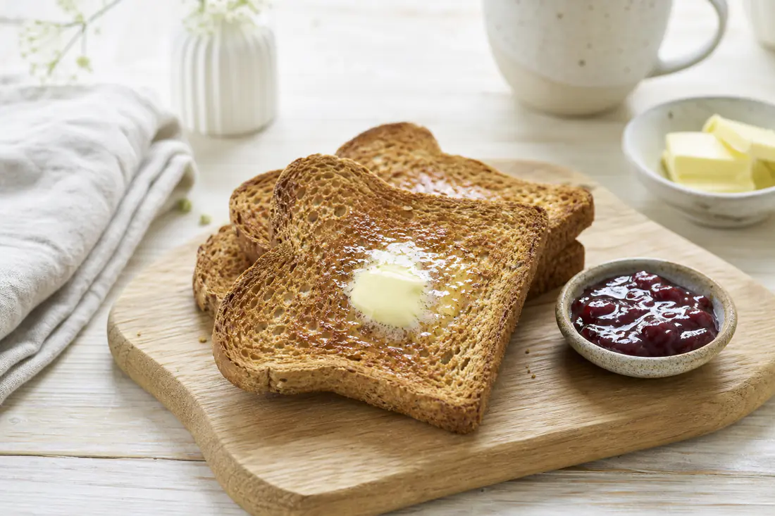 Goudbruine sneetjes geroosterd volkorenbrood met smeltende boter op een houten ontbijtplank