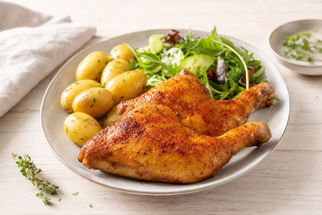 Twee goudbruine kippenbouten met krokant paprikavel op een bord met krieltjes en salade