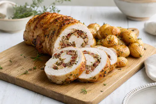 Goudbruine kiprollade in plakken gesneden met een gevuld, sappig snijvlak op een houten snijplank