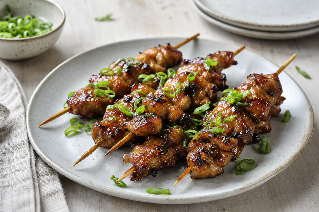 Kipspiesjes met glanzende ketjapmarinade op houten stokjes op een bord met lente-ui