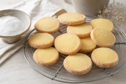 Ronde zandkoekjes met een rand van kristalsuiker op een rooster naast een schaaltje suiker