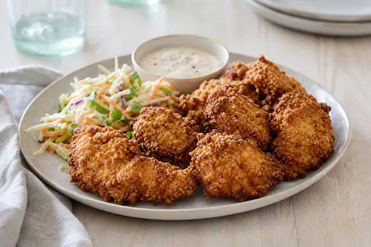 Goudbruine gepaneerde kipstukken met een ruwe, krokante korst op een bord met coleslaw en een schaaltje dip
