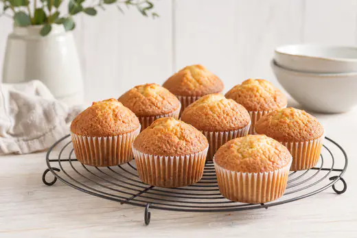 Goudbruine vanillemuffins met een gebarsten bolle bovenkant in papieren cups op een rooster