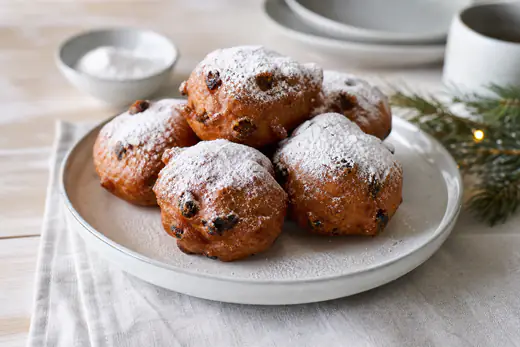 Opgewarmde oliebollen met krenten en een dikke laag poedersuiker op een wit bord