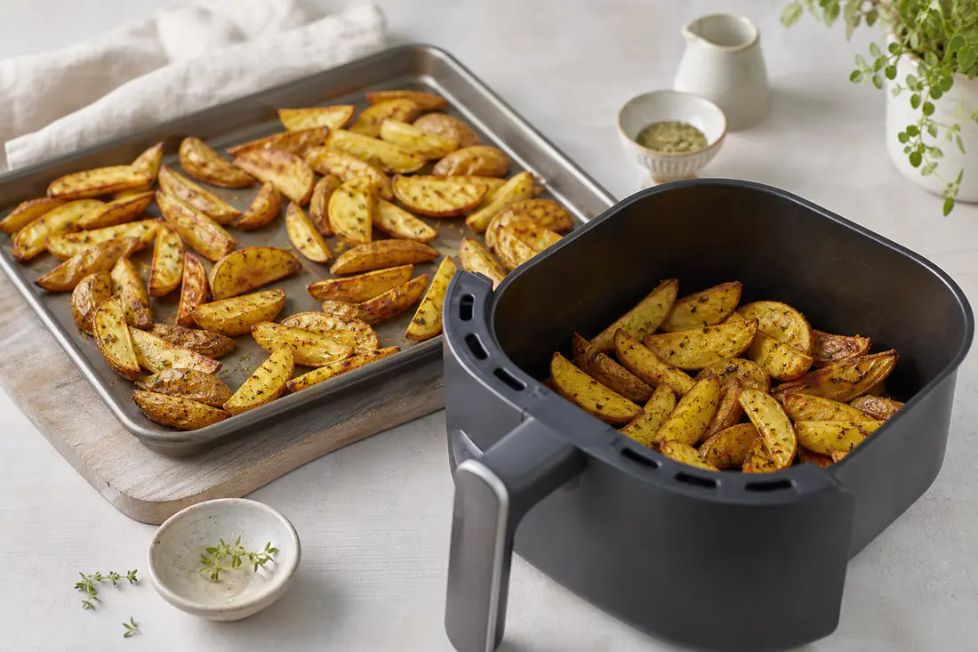 Bakplaat met aardappelpartjes naast een airfryermand met hetzelfde gerecht