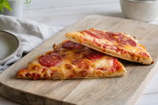 Twee opgewarmde pizzapunten met gesmolten kaas en salami op een houten plank, met een krokante bodem