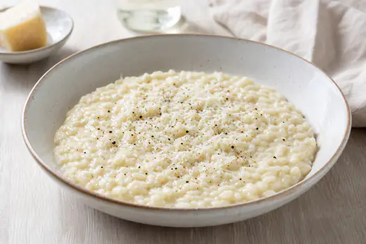 Romige Parmezaanrisotto in een diep bord met geraspte kaas en zwarte peper