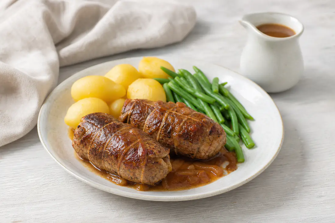 Twee bruingebakken rundervinken op een bord met gekookte aardappelen, sperziebonen en een schaaltje jus
