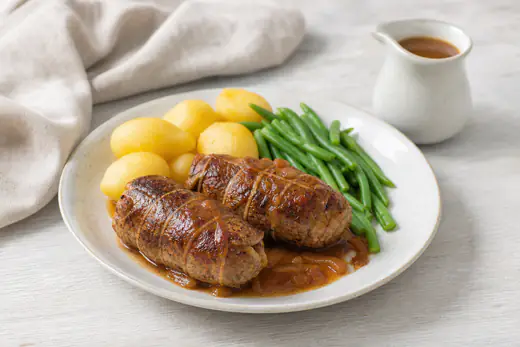 Twee bruingebakken rundervinken op een bord met gekookte aardappelen, sperziebonen en een schaaltje jus