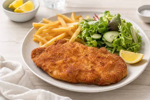 Goudbruine gepaneerde varkensschnitzel op een bord met een partje citroen, friet en een frisse salade