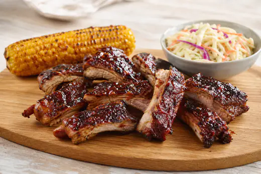 Glanzende spareribs met barbecueglaze, in stukken gesneden op een houten plank met maiskolf en coleslaw