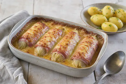 Gegratineerde witlof met ham en gesmolten kaas in een kleine ovenschaal